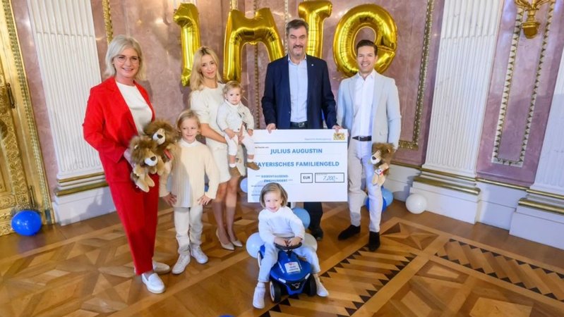 Archivbild: Im Oktober 2024 überreichten Sozialministerin Scharf und Ministerpräsident Söder der Familie des einmillionsten Kindes einen symbolischen Familiengeldscheck in Höhe von 7.200 Euro | Bild: Bayerische Staatskanzlei Archivbild: Im Oktober 2024 überreichten Sozialministerin Scharf und Ministerpräsident Söder der Familie des einmillionsten Kindes einen symbolischen Familiengeldscheck in Höhe von 7.200 Euro