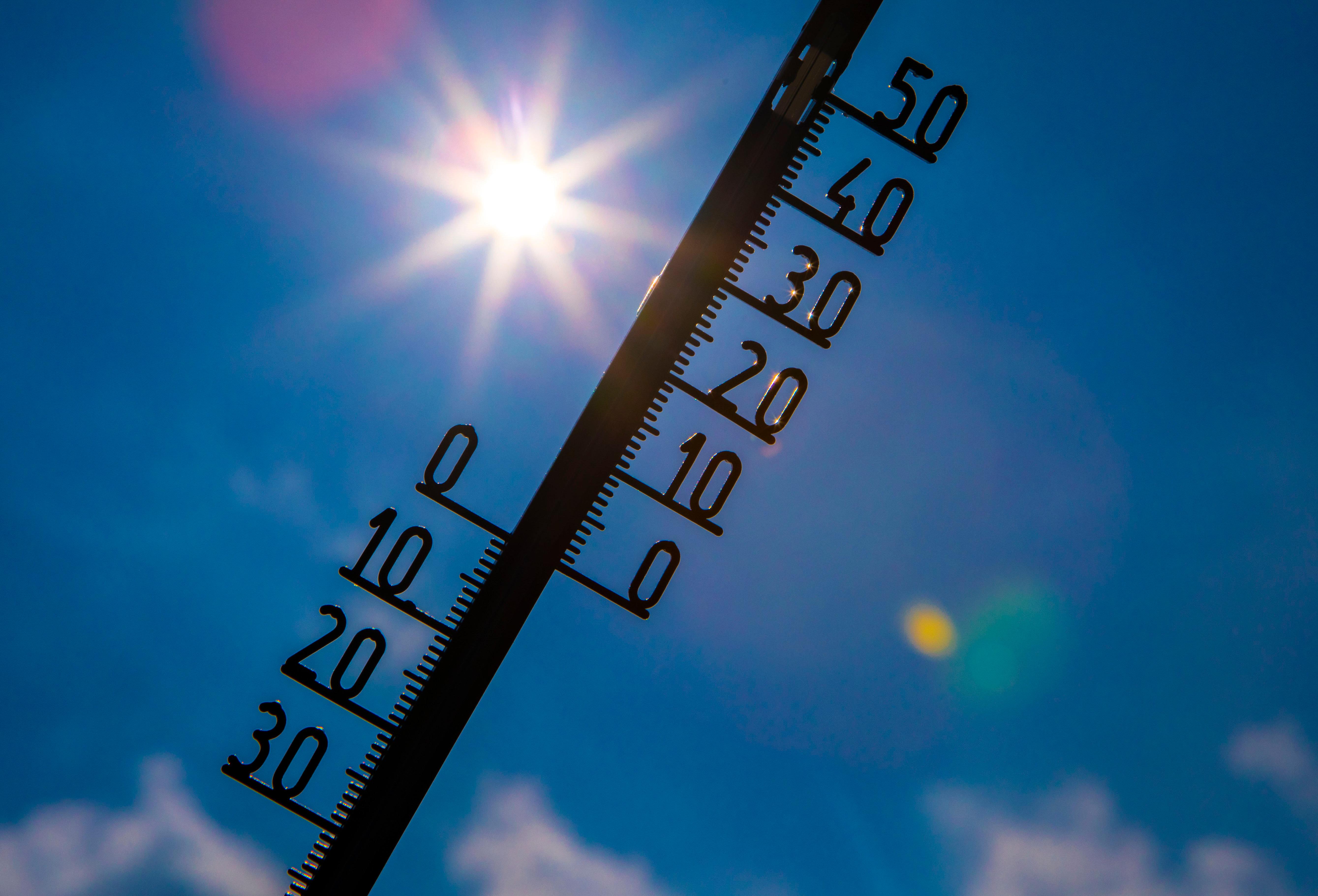Thermometer vor blauem Himmel und Sonne 
