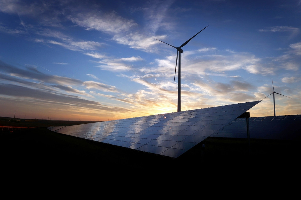 02.06.2021, Bayern, Kitzingen: Windräder stehen hinter den Solarzellen einer Solarkraftanlage. 