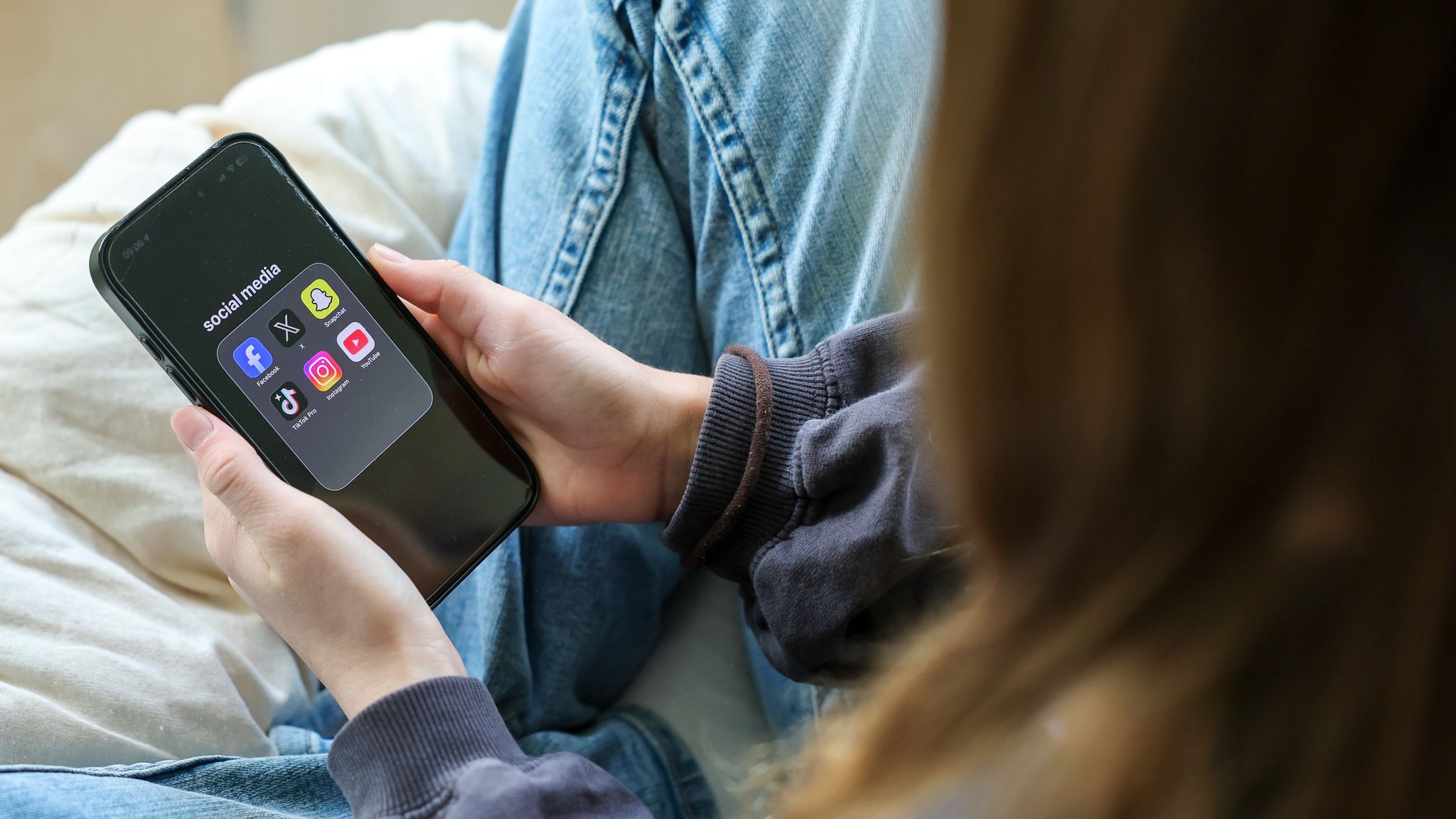 ILLUSTRATION - 24.09.2026, Sachsen, Leipzig: Ein Mädchen hält ein iPhone 16 in den Händen, auf dessen Display in einem Ordner mit der Bezeichnung „social media“ die Logos von Facebook, X (ehemals Twitter), Snapchat, TikTok Pro, Instagram und YouTube zu sehen sind. (zu dpa: «Griechenland: Social-Media-Verbot für U-15-Jährige kommt») Foto: Jan Woitas/dpa +++ dpa-Bildfunk +++