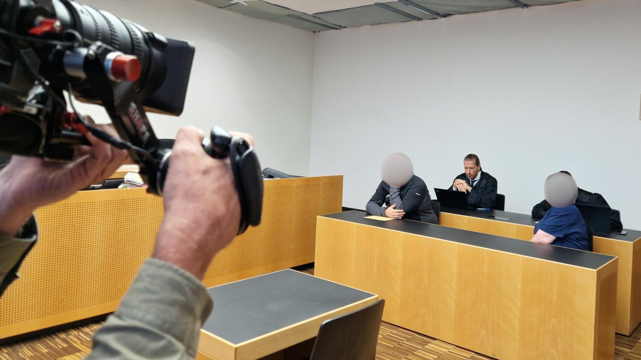 Die Angeklagten sitzen auf der Anklagebank, hinter ihnen ihre Anwälte, im Vordergrund Kameras.