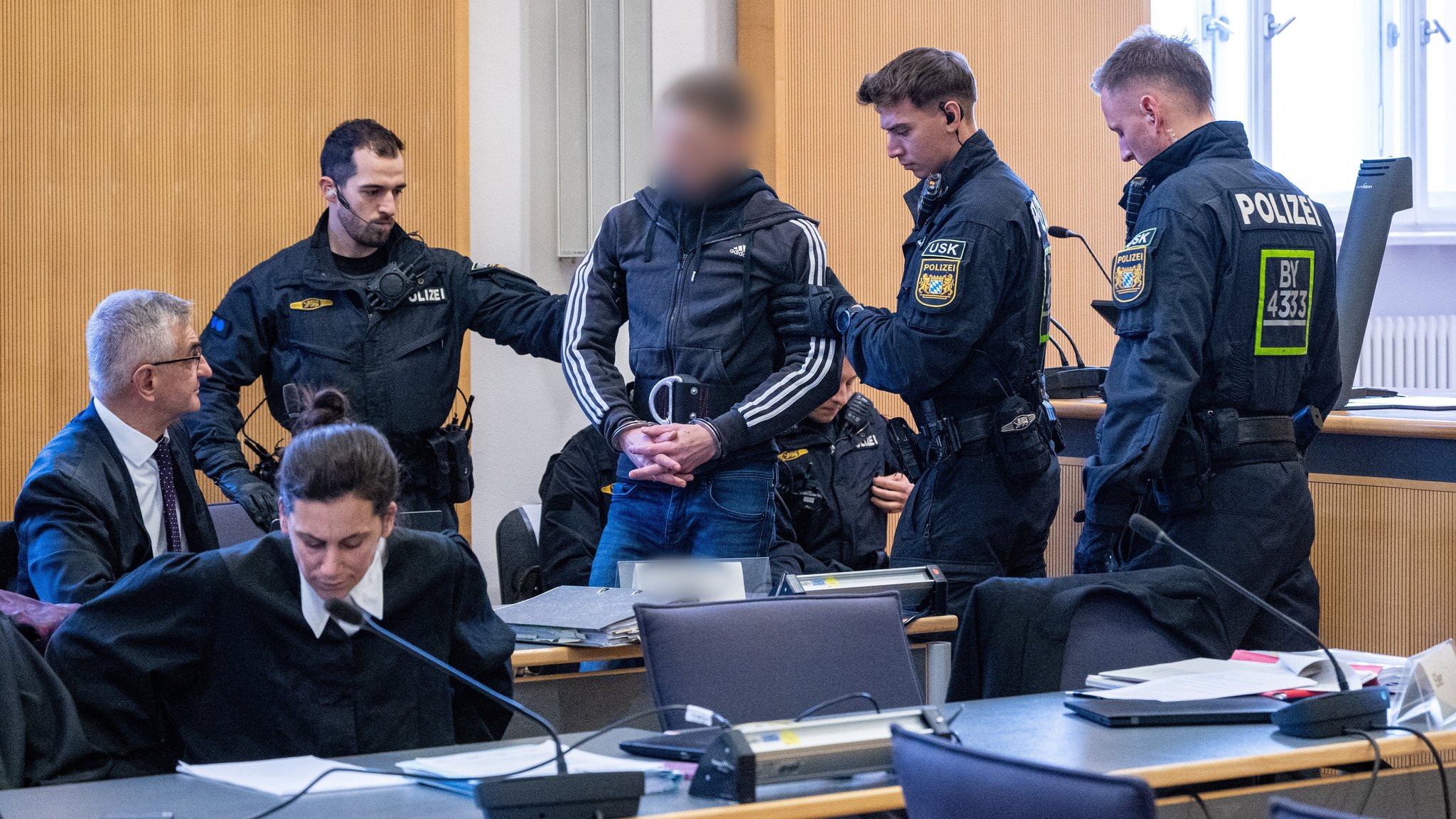 Zu Prozessbeginn im Dezember 2025 wird einer der vier Angeklagten von mehreren Polizisten in den Verhandlungssaal des Landgerichts Regensburg geführt. 