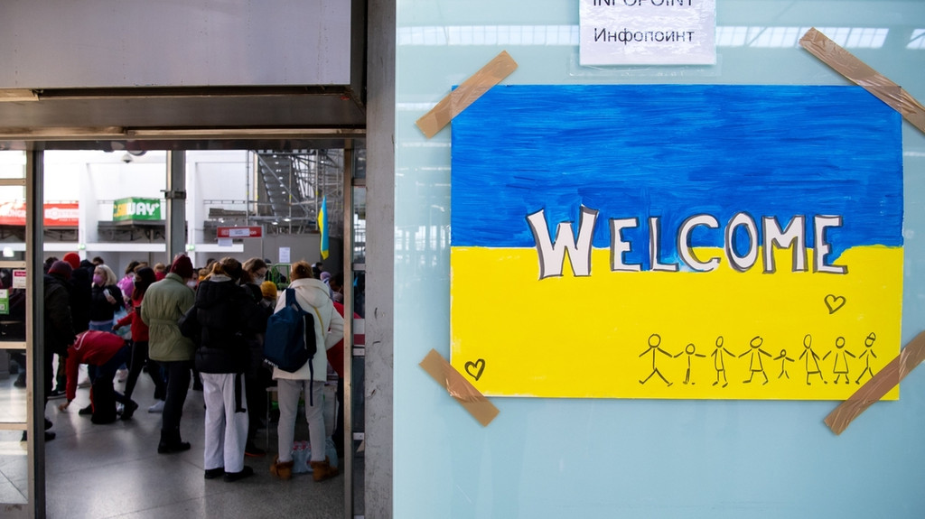 ARCHIV - 09.03.2022, Bayern, München: Ein Schild in den Farben der Ukraine mit der Aufschrift "Welcome" ist am Hauptbahnhof zu sehen. Im Hintergrund werden Flüchtlinge aus der Ukraine nach ihrer Ankunft von Mitarbeitern der Caritas und freiwilligen Helfern empfangen. Doch auch im vermeintlich sicheren Deutschland drohen Gefahren. Hilfsorganisationen warnen, dass geflüchtete Frauen Opfer von Zwangsprostitution oder Ausbeutung werden könnten und setzen deshalb auf Aufklärung. (zu dpa «Ausbeutung oder gar Gewalt - Wenn geflüchtete Frauen zu Opfern werden») Foto: Sven Hoppe/dpa +++ dpa-Bildfunk +++ | Bild: dpa-Bildfunk/Sven Hoppe ARCHIV - 09.03.2022, Bayern, München: Ein Schild in den Farben der Ukraine mit der Aufschrift "Welcome" ist am Hauptbahnhof zu sehen. Im Hintergrund werden Flüchtlinge aus der Ukraine nach ihrer Ankunft von Mitarbeitern der Caritas und freiwilligen Helfern empfangen. Doch auch im vermeintlich sicheren Deutschland drohen Gefahren. Hilfsorganisationen warnen, dass geflüchtete Frauen Opfer von Zwangsprostitution oder Ausbeutung werden könnten und setzen deshalb auf Aufklärung. (zu dpa «Ausbeutung oder gar Gewalt - Wenn geflüchtete Frauen zu Opfern werden») Foto: Sven Hoppe/dpa +++ dpa-Bildfunk +++
