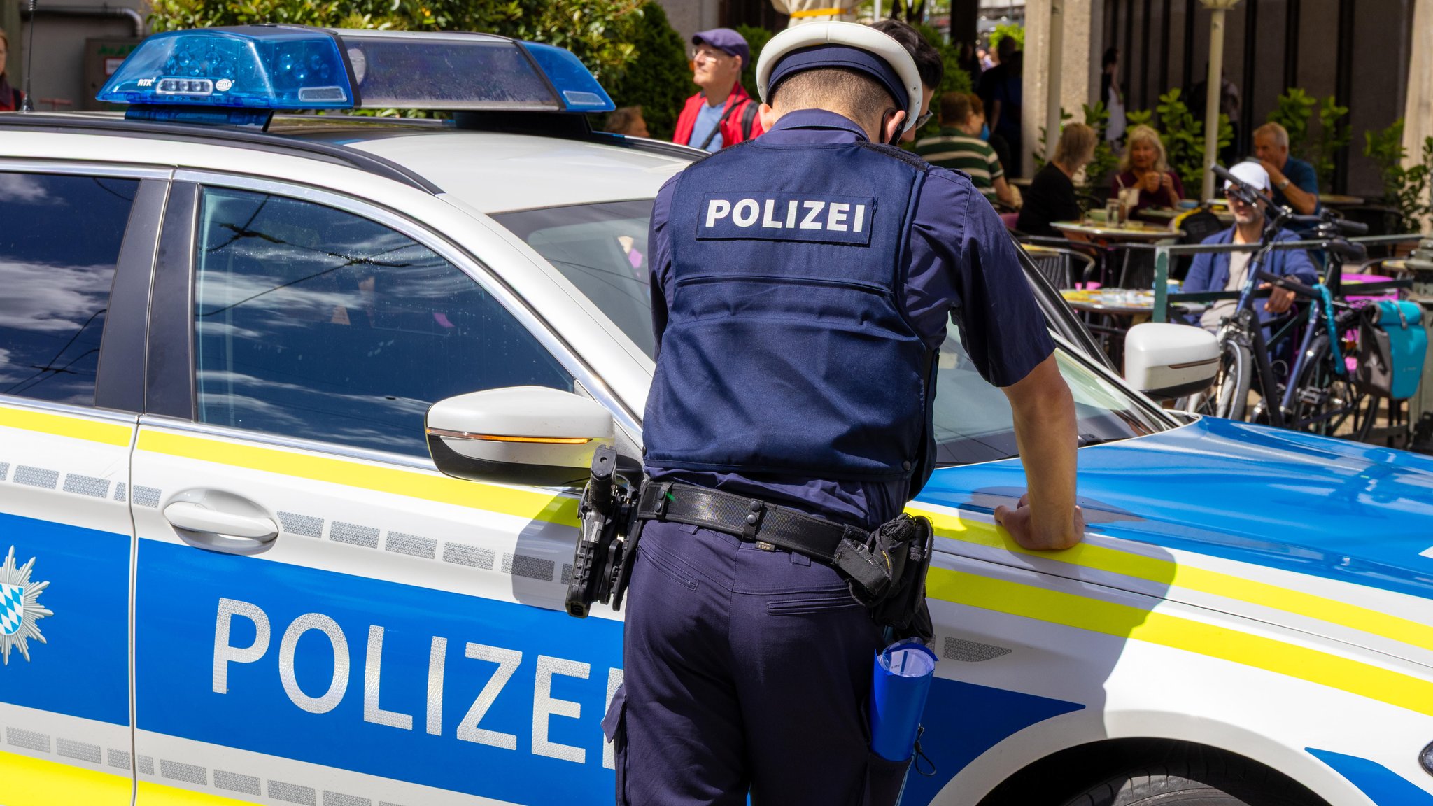 (Symbolbild) Polizist an einem Streifenwagen der Bayerischen Polizei im Stadtgebiet von Augsburg