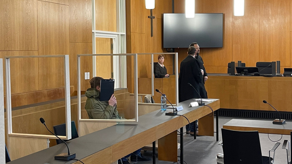 Der Angeklagte verdeckt im Gerichtssaal sein Gesicht