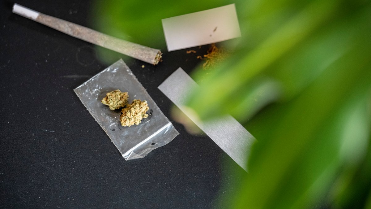 Auf einem Tisch liegt ein Joint, eine Cannabisblüte und weiteres Zubehör für den Konsum (Symbolbild).