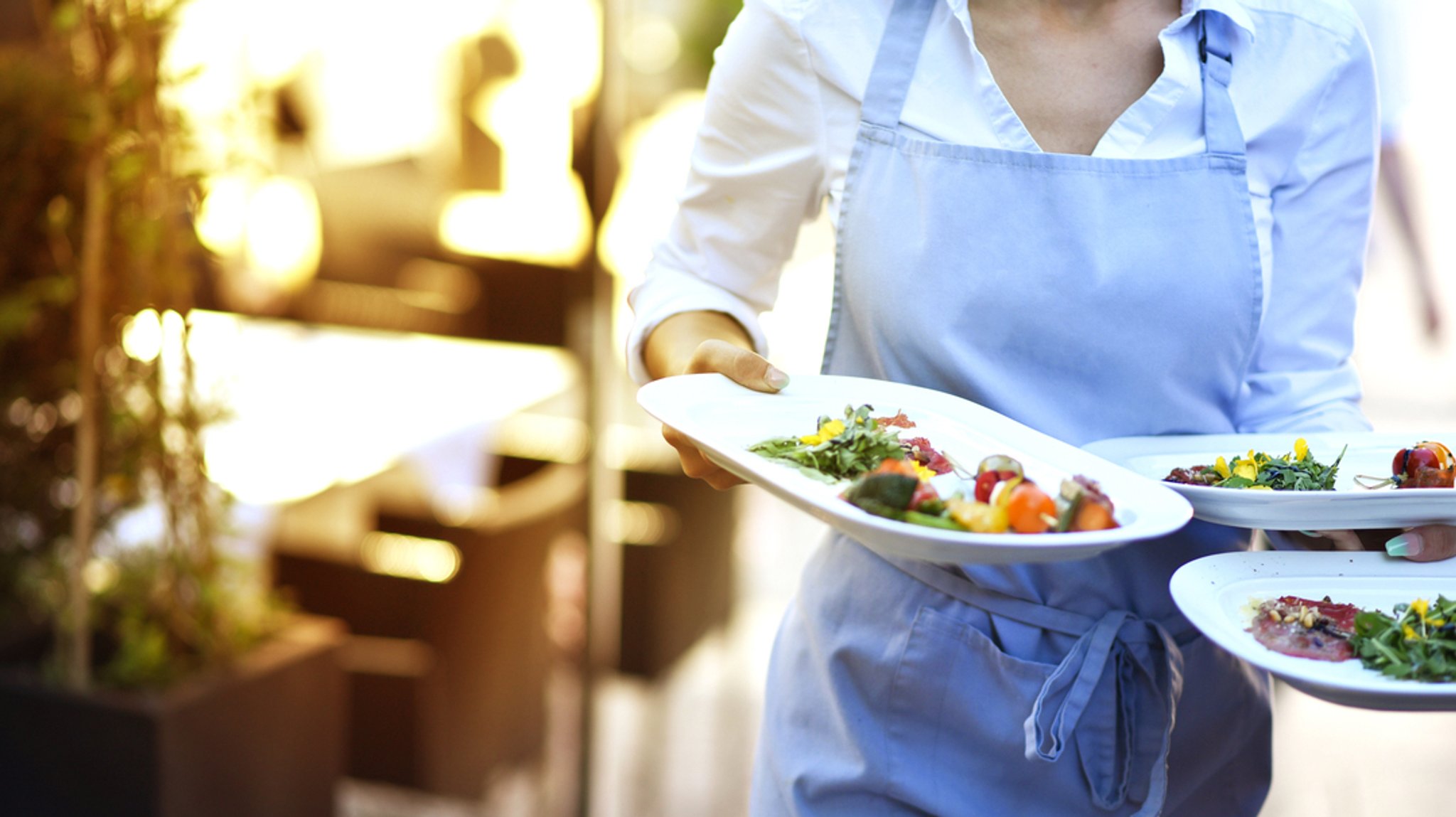 Minijob (Symbolbild): Eine Kellnerin trägt im Außenbereich eines Restaurants drei Speisen. | Bild: stock.adobe.com/s-motive Minijob (Symbolbild): Eine Kellnerin trägt im Außenbereich eines Restaurants drei Speisen.