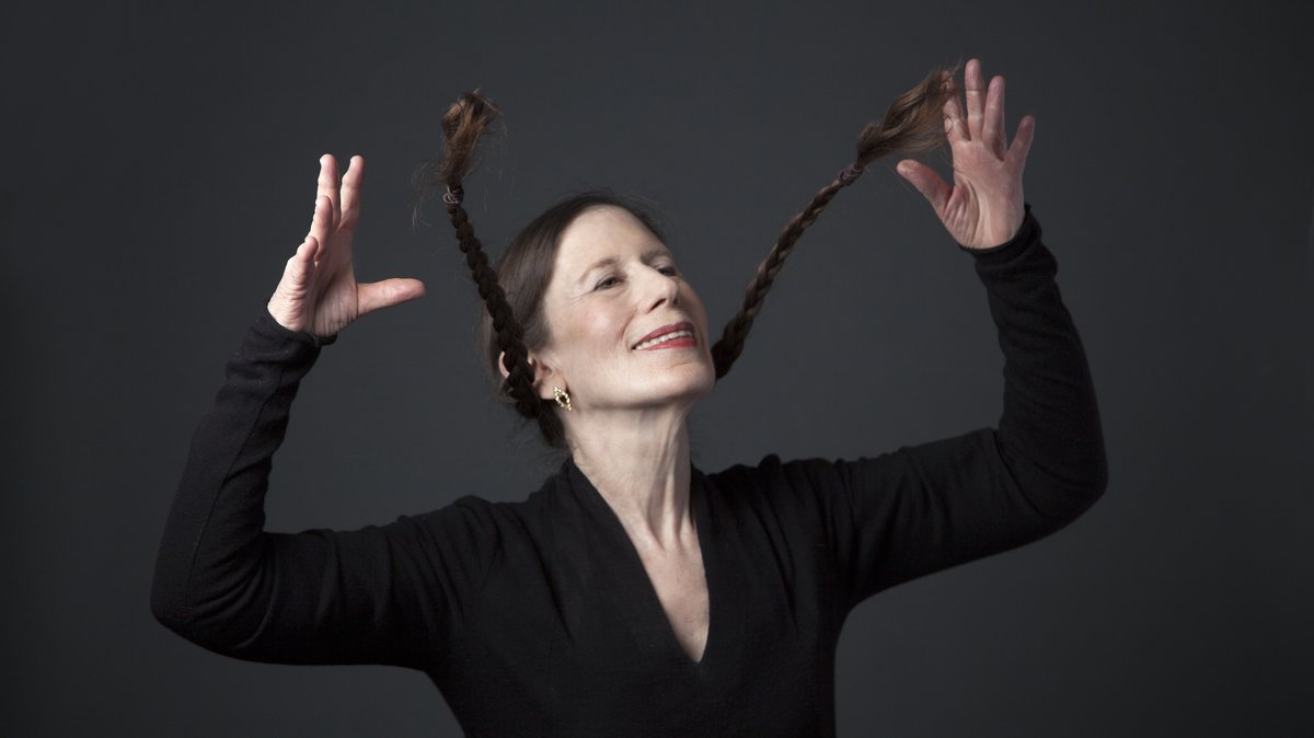 Frau in Schwarz wirft schwungvoll ihre langen, geflochtenen Zöpfe durch die Luft
