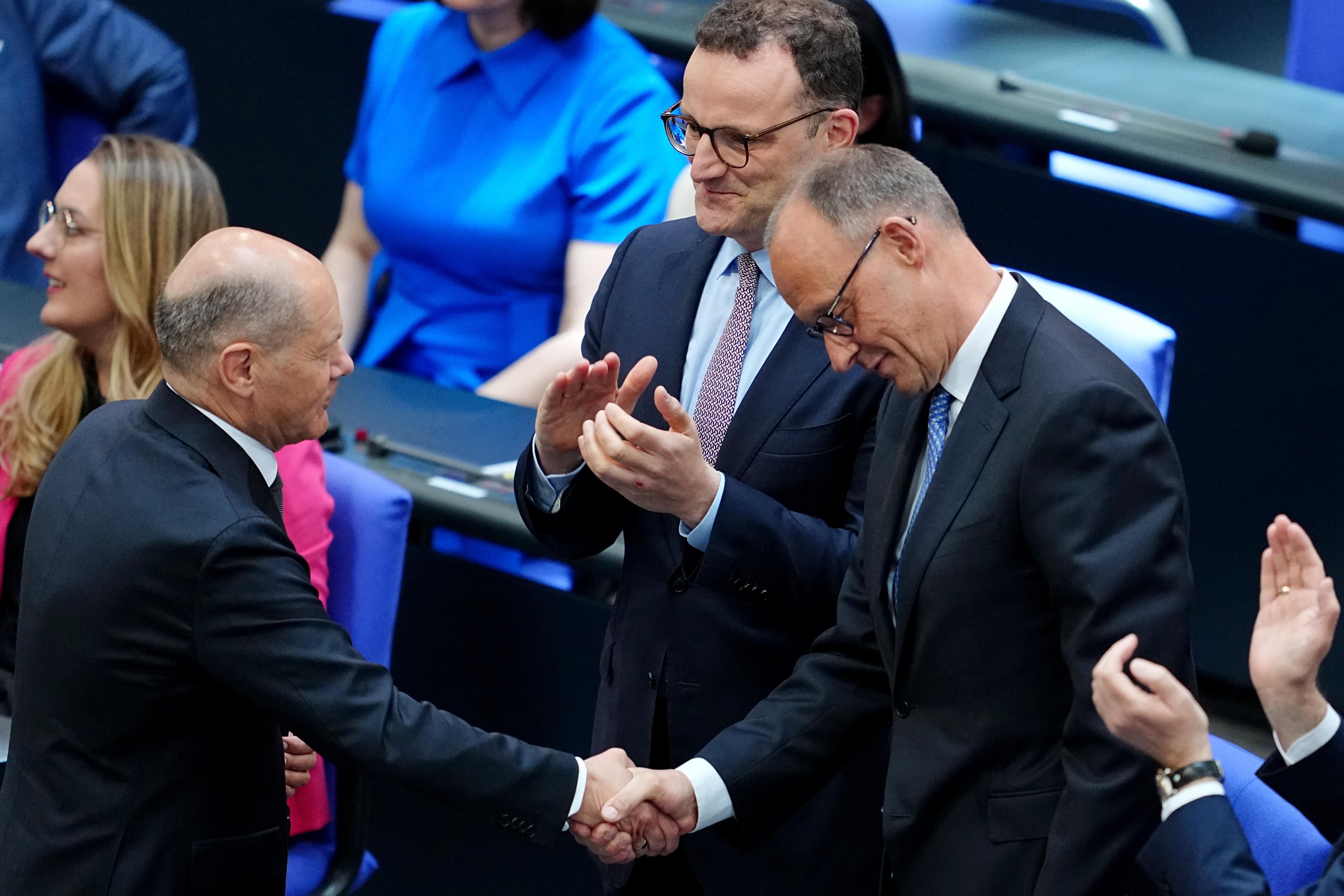 Der neue Bundeskanzler Merz (CDU, r.) und der geschäftsführende Bundeskanzler Scholz (SPD, l.) neben Unions-Fraktionschef Spahn im Bundestag.