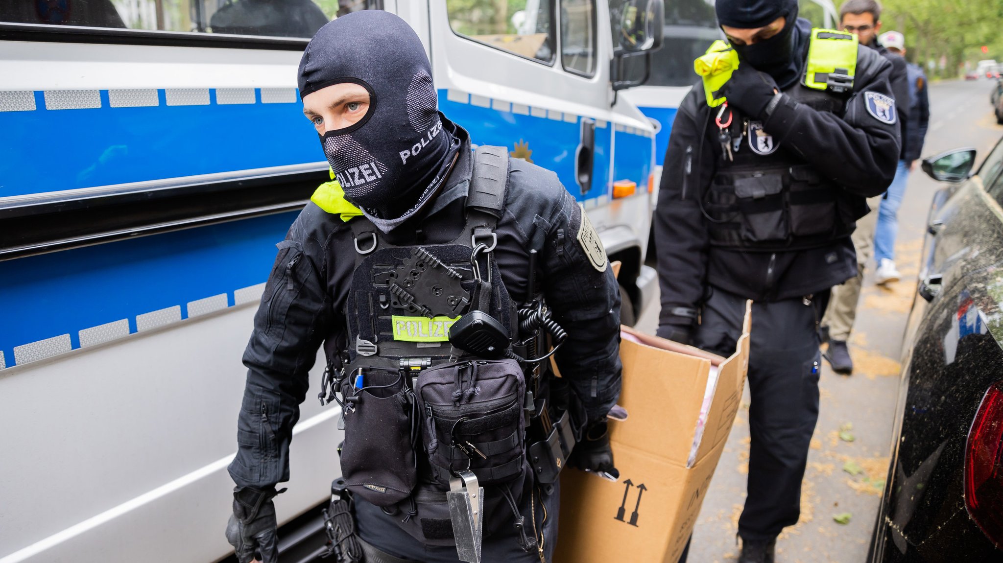 Polizisten tragen bei der Razzia in Berlin-Kreuzberg einen Karton zu einem Fahrzeug.