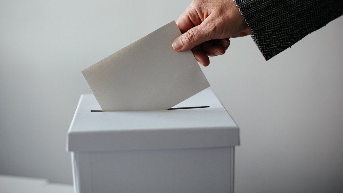 Ein Mensch wirft einen Wahlschein in eine Wahlurne (Symbolbild)