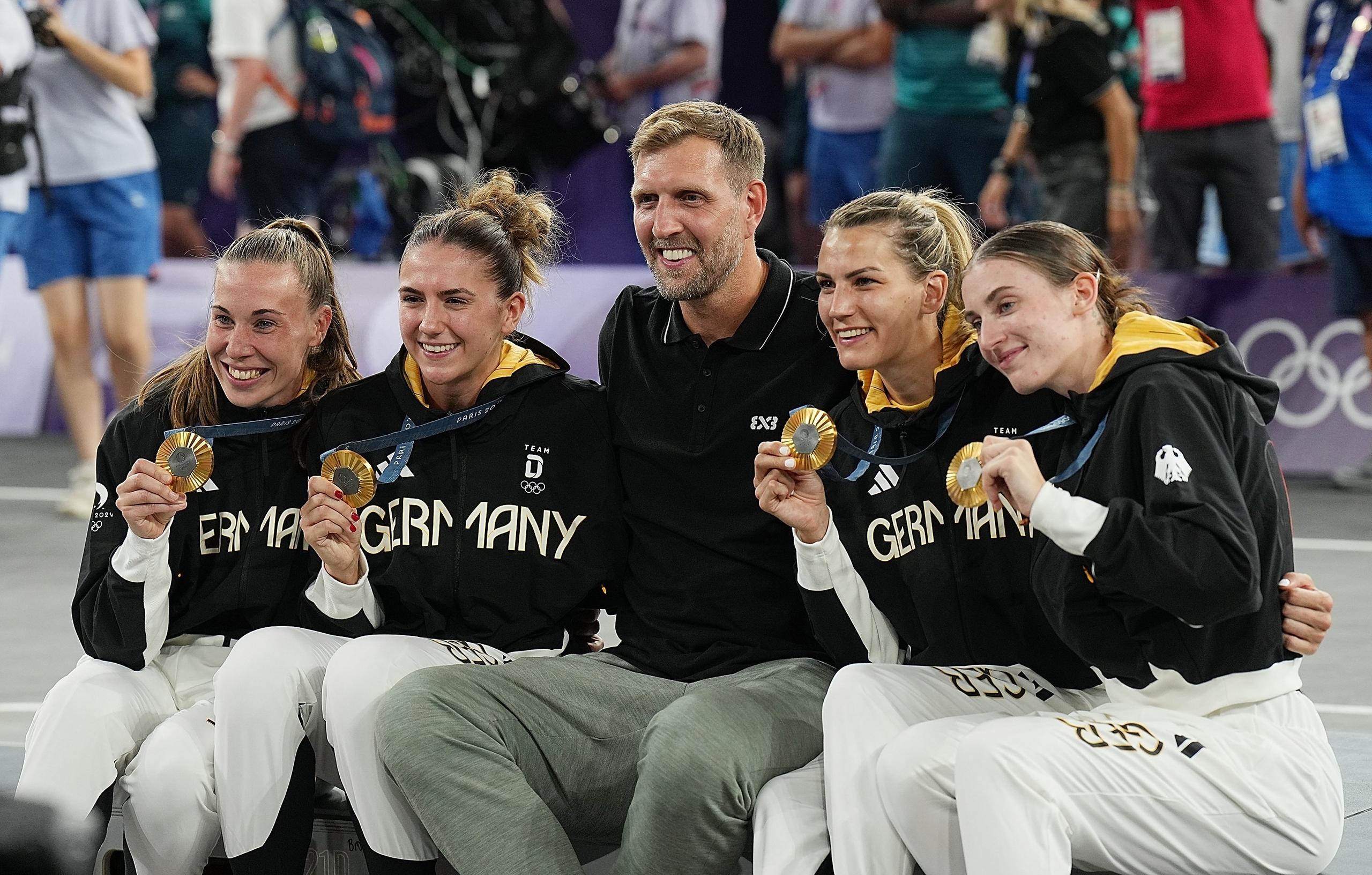 ARCHIV - 05.08.2024, Frankreich, Paris: Olympia, Paris 2024, 3x3 Basketball, Damen, Finale, Deutschland - Spanien, Finalrunde, Place de la Concorde, der ehemalige NBA-Star Dirk Nowitzki feiert mit die Goldmedaillengewinnerinnen Svenja Brunckhorst (l-r), Marie Reichert, Sonja Greinacher und Elisa Mevius nach der Siegerehrung. (zu dpa: «Excel und Abwärtstrend: Deutscher Sport im Olympia-Tief») 