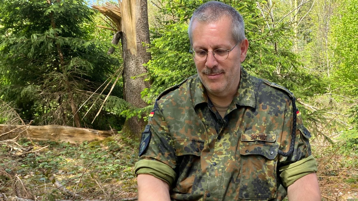 Ein Bundeswehrsoldat sitzt mit seinem Assistenzhund auf einem Baumstamm im Wald.