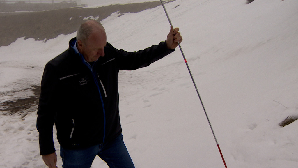 Ein Mann testet mit einem Stab, wieviel Schnee am Tegelberg liegt. 