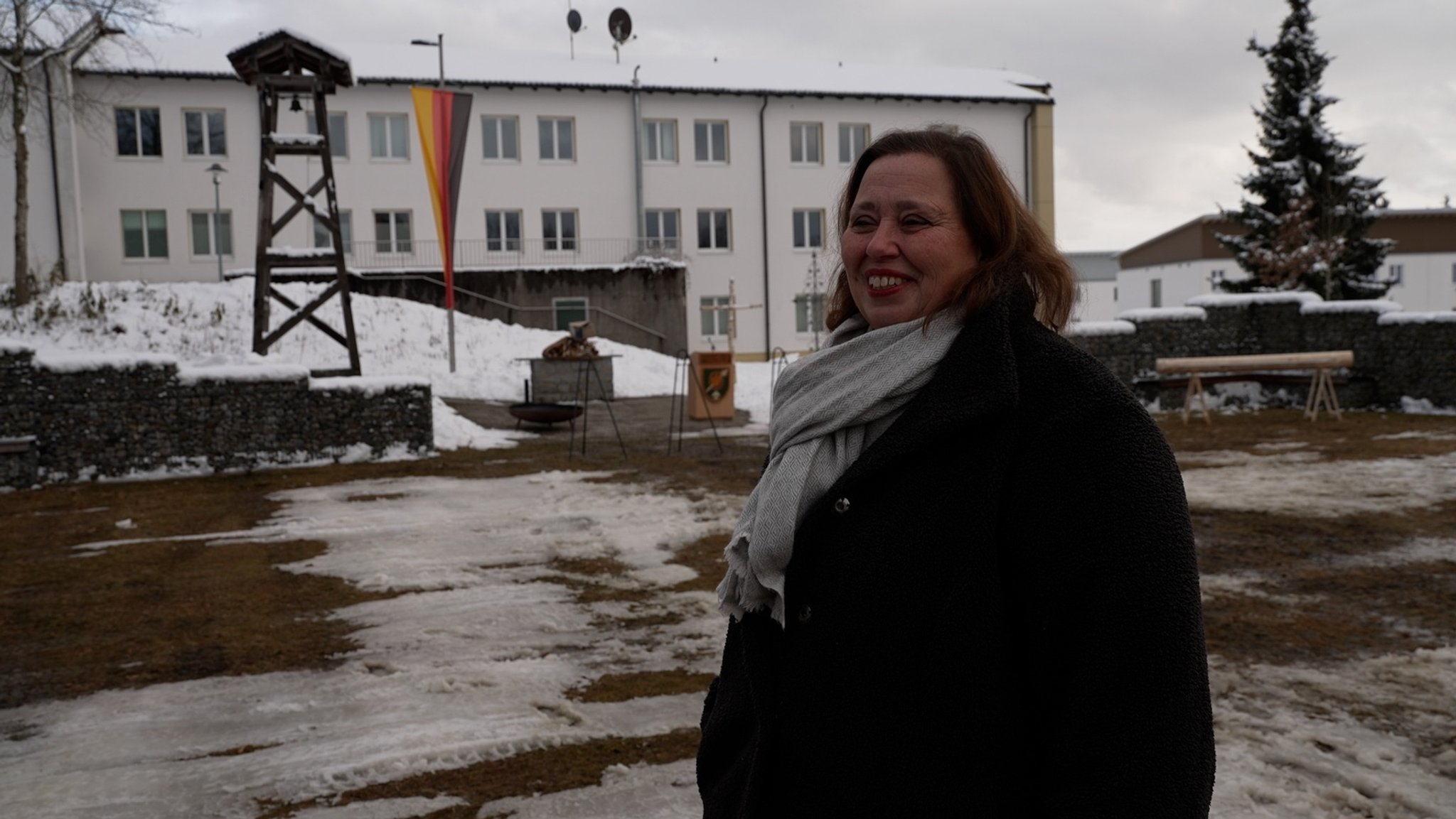 Eine Frau steht bei einer Bundeswehrkaserne. Im Hintergrund ist eine Deutschlandfahne zu sehen.