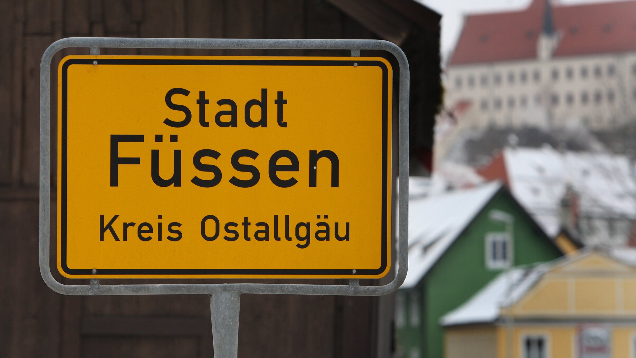 Ein Ortsschild von Füssen, Im Hintergrund schneebedeckte Hausdächer | Bild: picture-alliance/ dpa | Karl-Josef Hildenbrand Ein Ortsschild von Füssen, Im Hintergrund schneebedeckte Hausdächer