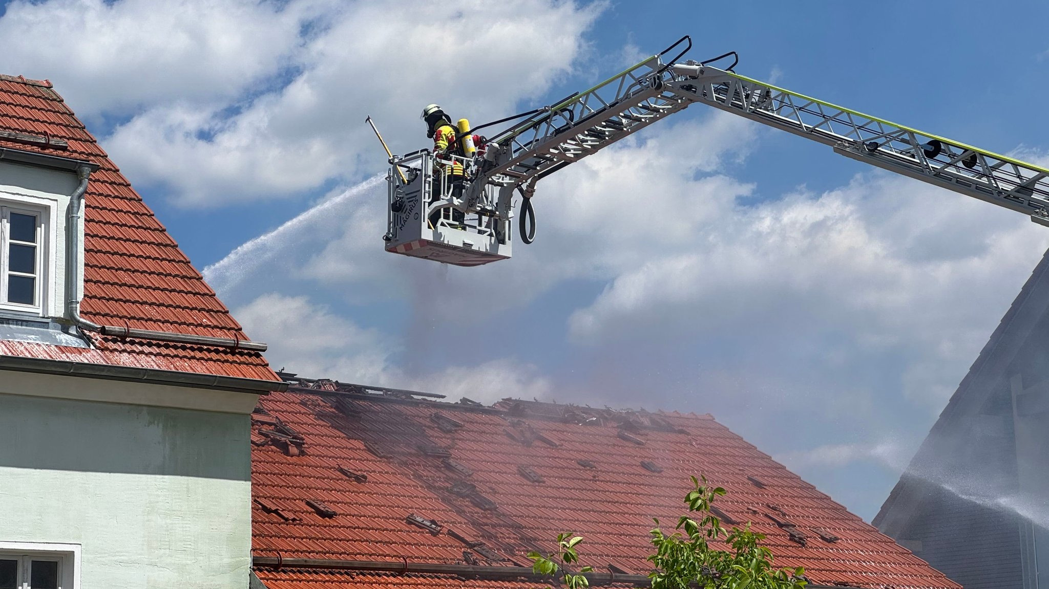 Feuerwehrkräfte spritzen von der Drehleiter in den Dachstuhl der brennenden Scheune.