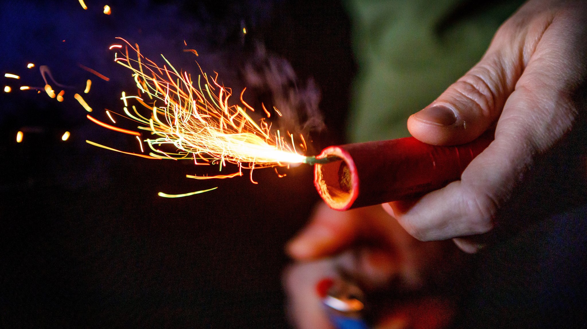 Ein Mensch zündet eine Feuerwerks-Rakete an, es fliegen Feuerfunken.