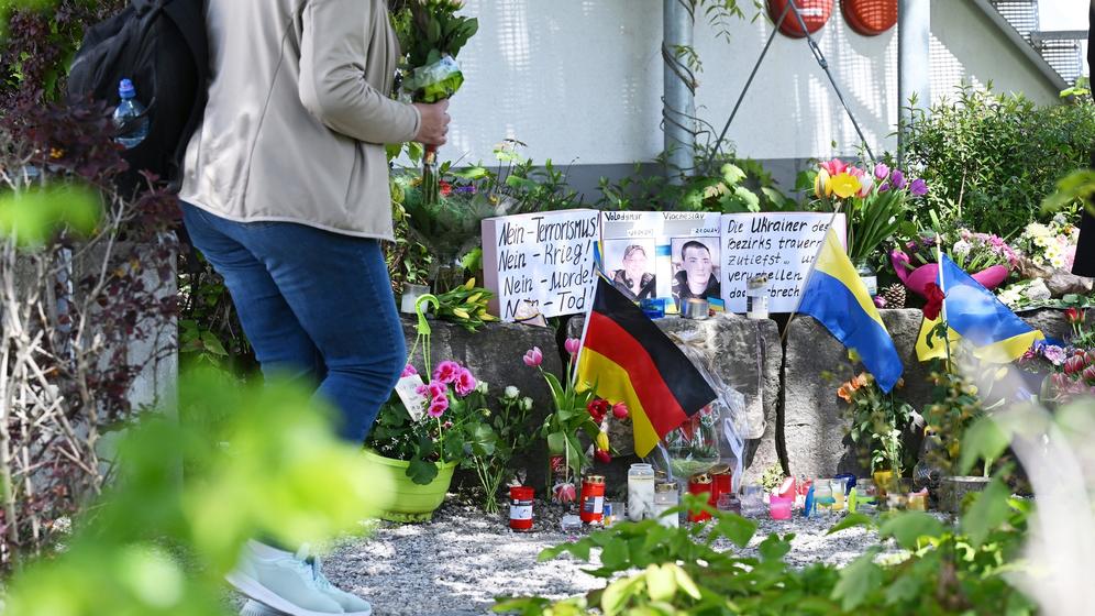 29.04.2024, Murnau Am Staffelsee: Neben dem Einkaufszentrum an dem am Samstagabend zwei Männer aus der Ukraine getötet worden sind, haben Menschen Blumen und Plakate niedergelegt. Die beiden getötete Ukrainer waren Armeeangehörige. Foto: Angelika Warmuth/dpa - ACHTUNG: Namen wurden aus rechtlichen Gründen gepixelt +++ dpa-Bildfunk +++ | Bild:dpa-Bildfunk/Angelika Warmuth