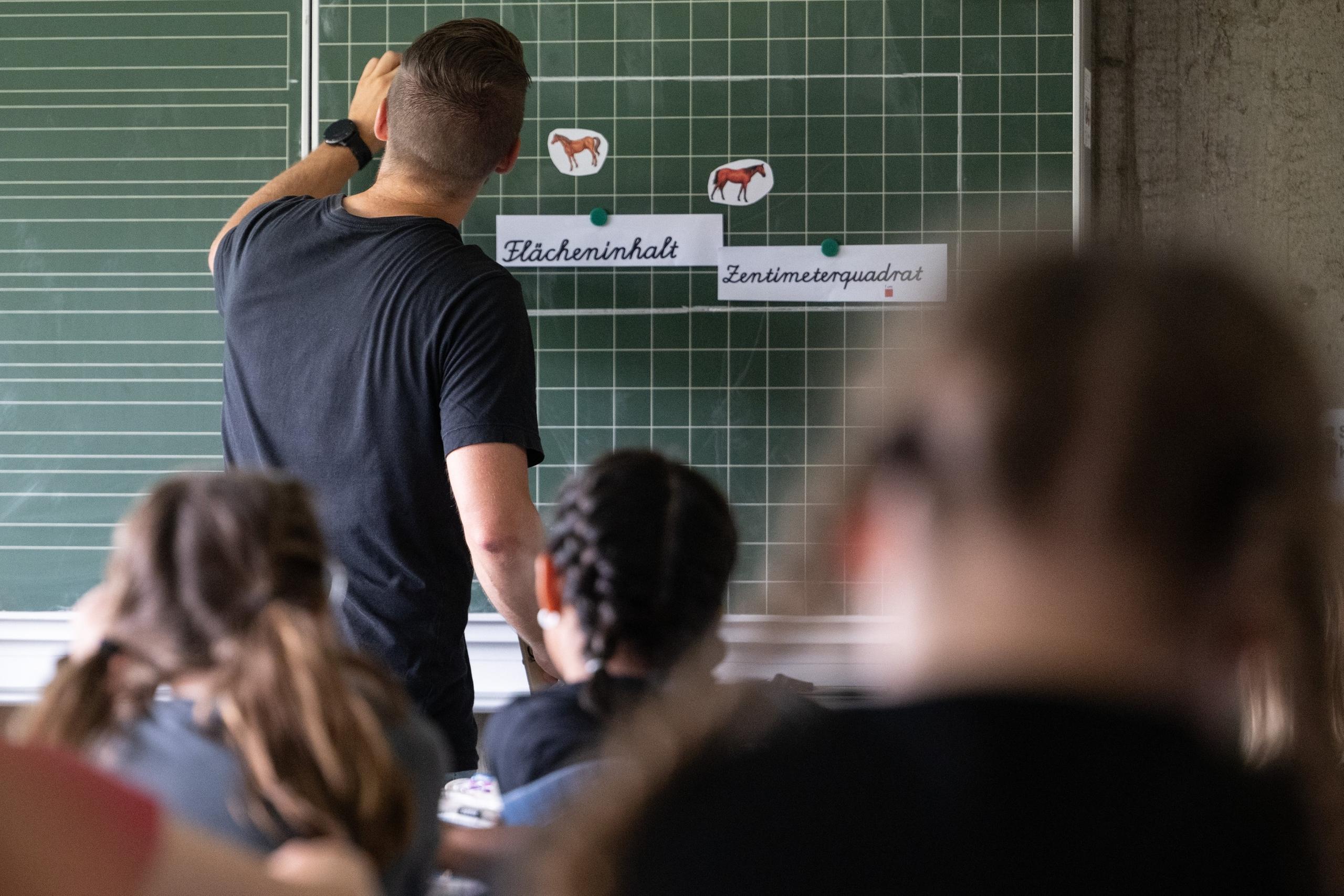 PRODUKTION - 27.06.2024, Baden-Württemberg, Neckartailfingen: Ein Lehrer macht im Unterricht einer vierten Klasse einer Grundschule einen Tafelanschrieb, während an der Tafel Zettel mit der Aufschrift «Flächeninhalt» und «Zentimeterquadrat» hängen. (zu dpa: «Hamburg vermeldet Rekord bei neu eingestellten Lehrkräften») Foto: Marijan Murat/dpa +++ dpa-Bildfunk +++
