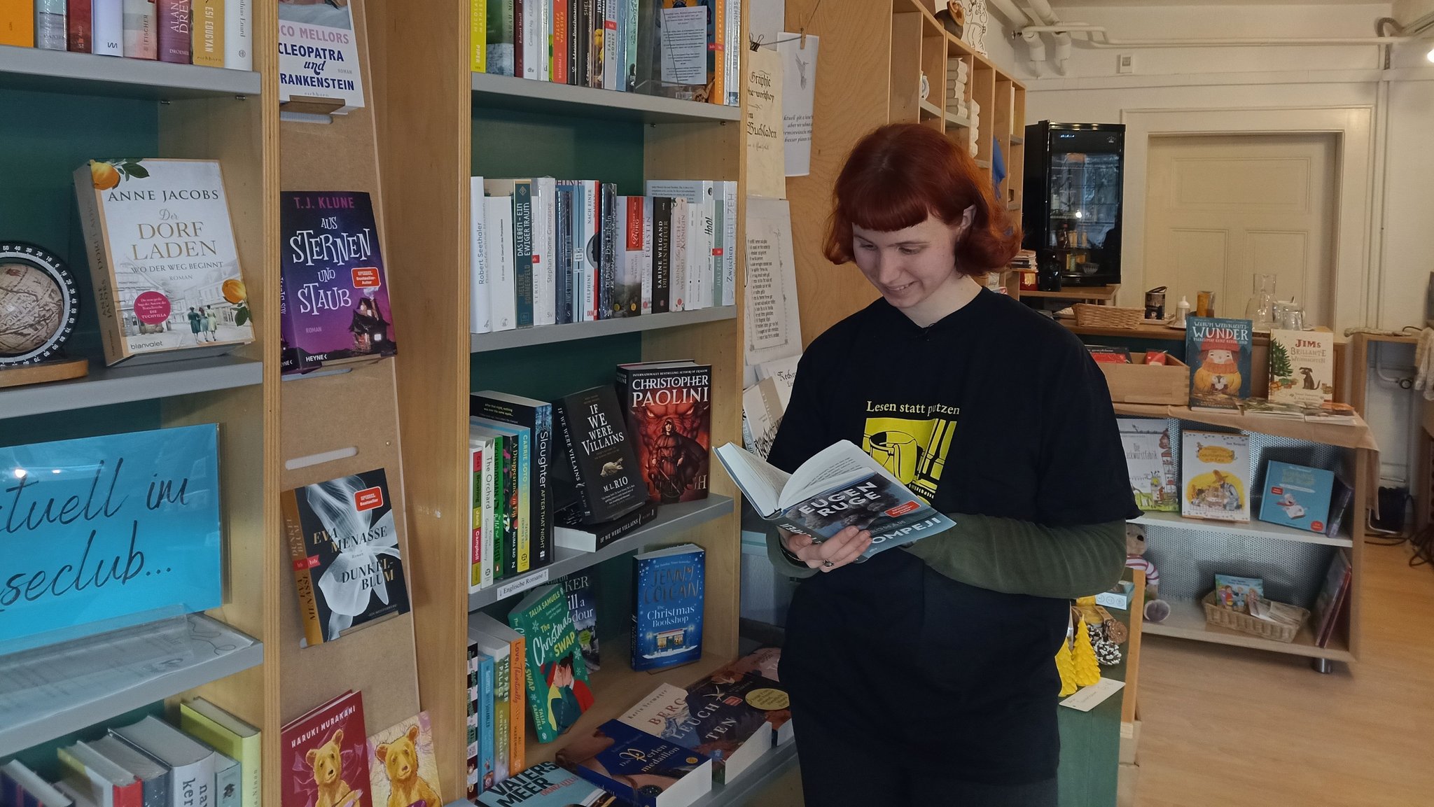 Junge Frau steht an einem Bücherregal und liest in einem Buch.