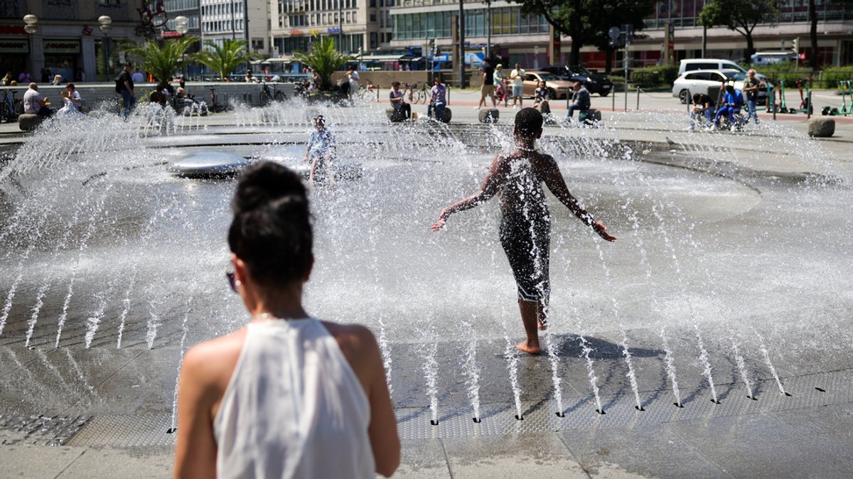 Ein Junge erfrischt sich bei sommerlichen Temperaturen im Wasserspiel am Stachus in der Innenstadt von München.