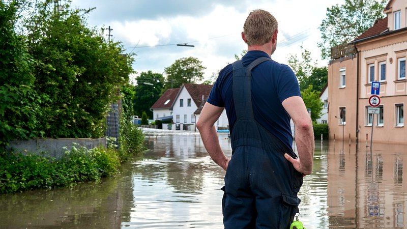 Ein Einsatzhelfer steht vor einer mit Hochwasser überfluteten Wohngegegend in Günzburg und sieht sich das Ausmaß an.