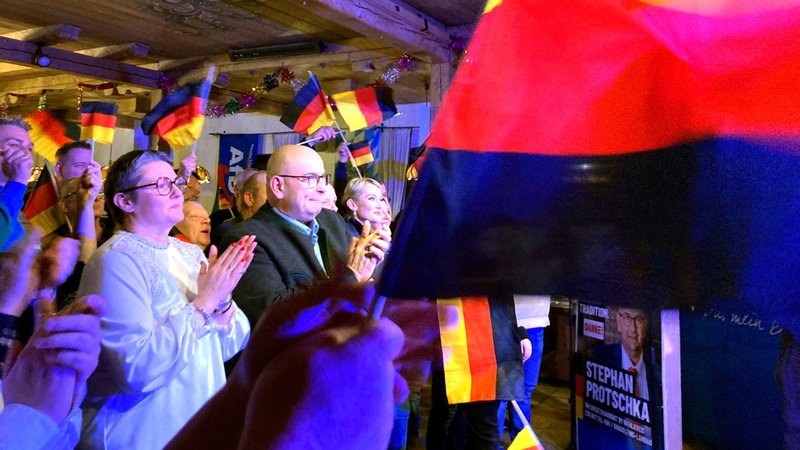 Die AfD hat sich vor einem Bildschirm versammelt und schwenkt Deutschlandfahnen. | Bild: dpa-Bildfunk/Sabine Dobel Die AfD hat sich vor einem Bildschirm versammelt und schwenkt Deutschlandfahnen.