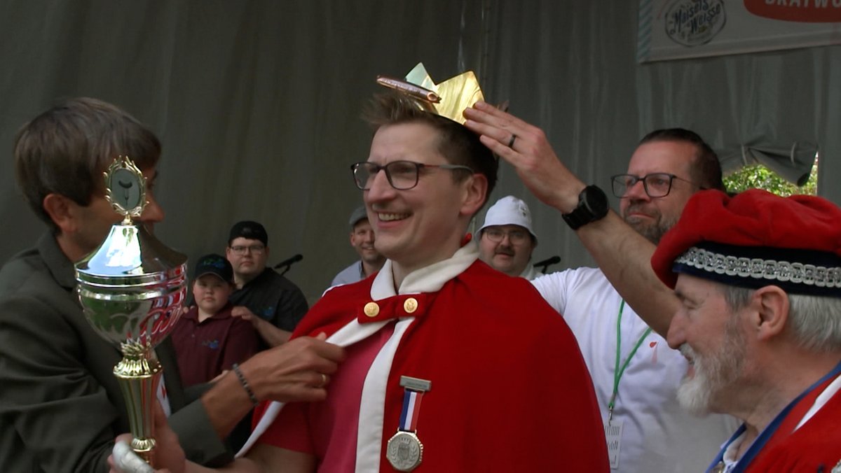 Der Bratwurstkönig Dirk Freyberger hält einen Pokal und bekommt eine Krone aufgesetzt. 