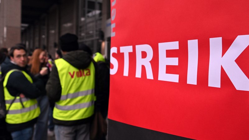 Rotes Transparent mit dem Wort "Streik", daneben Beschäftigte mit gelber Streikweste.