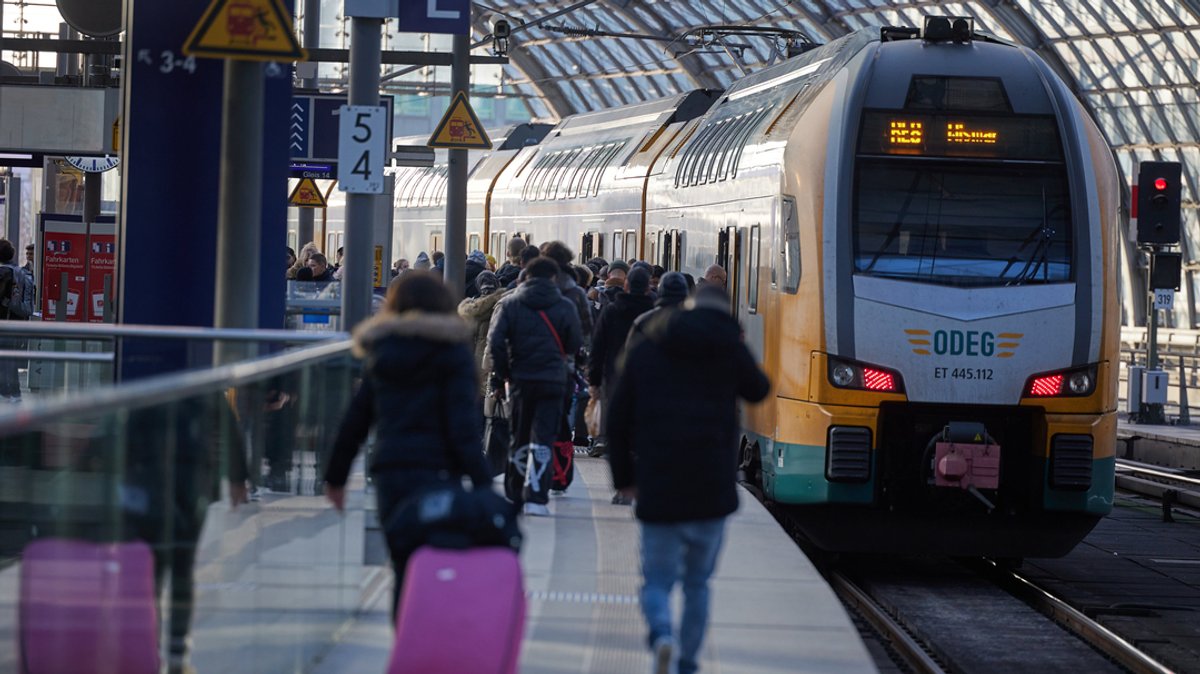 27.01.2024, Berlin: Reisende gehen im Hauptbahnhof auf einem Gleis neben einem Zug der ODEG-Linie RE 8 nach Wismar entlang.