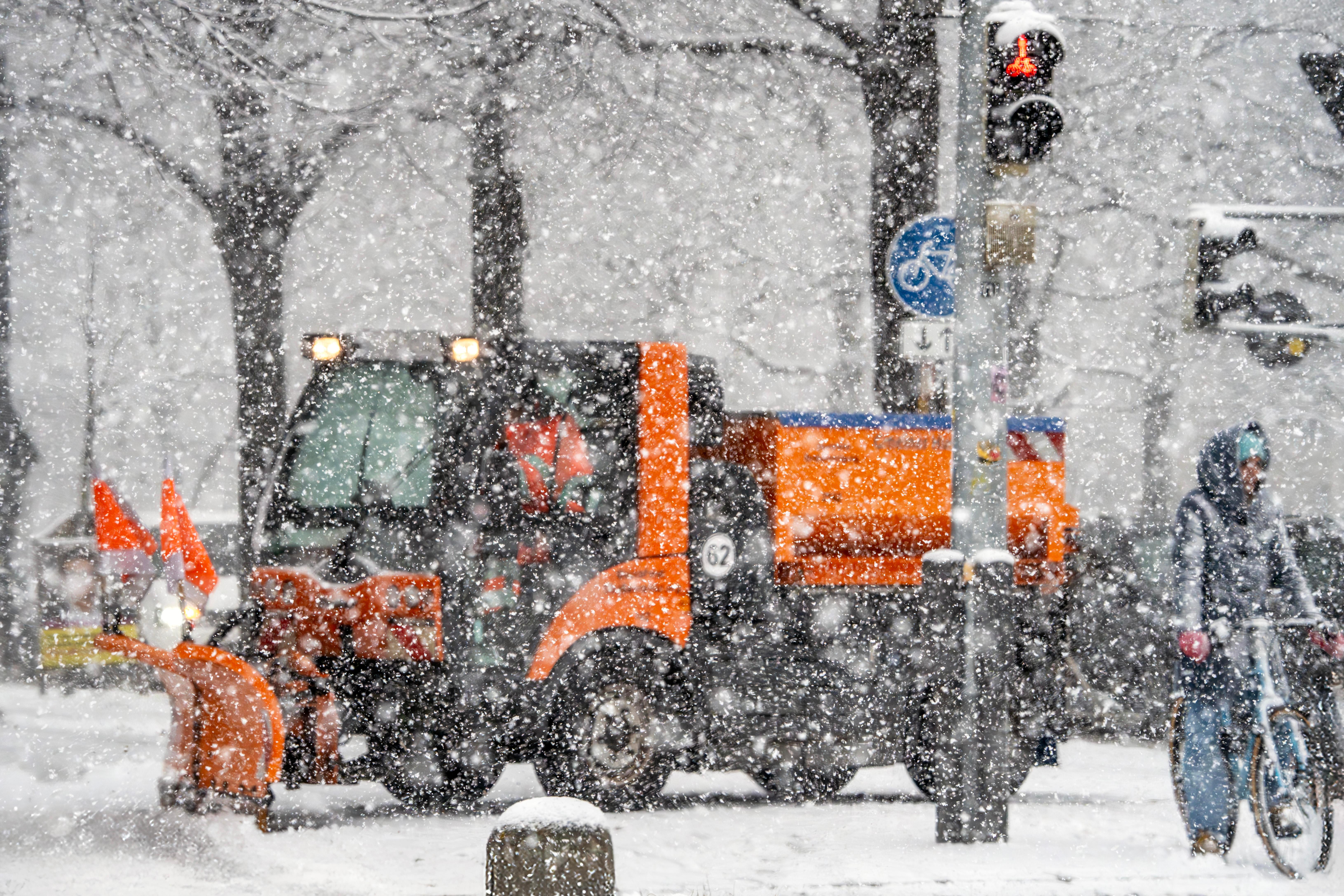 Ein orangefarbenes Räumfahrzeug ist im dichten Schneetreiben nur schemenhaft zu erkennen.