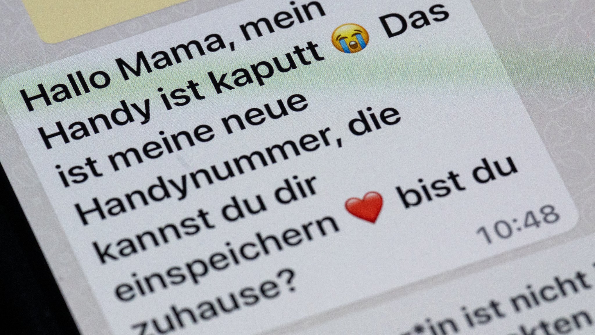 Auf dem Display eines Smartphones steht eine Whats App-Nachricht, die im Tonfall betrügerischen Nachrichten nachempfunden ist, die dazu genutzt werden, Geld zu bekommen.