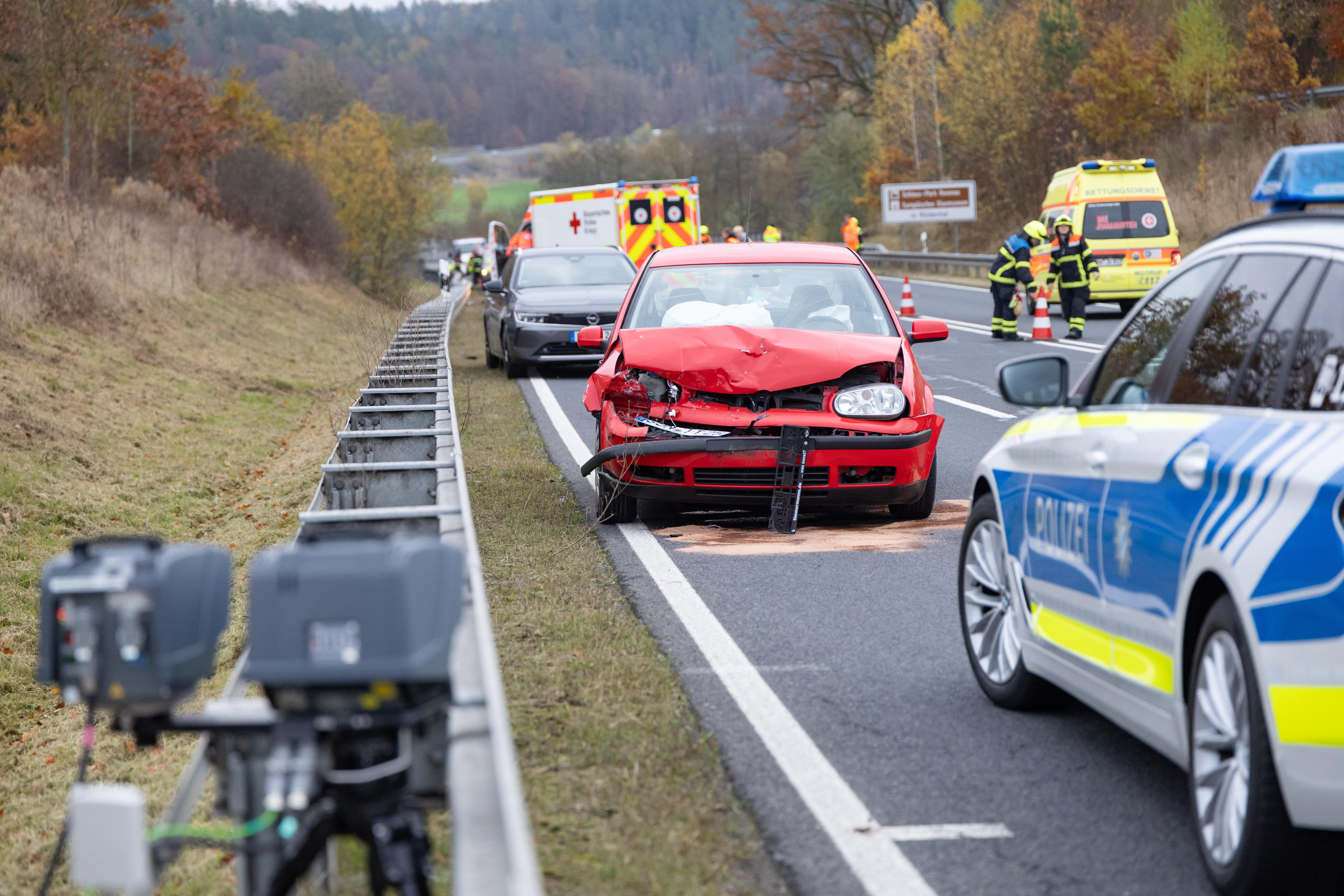 Einsatzkräfte von Polizei und Rettungsdienst stehen neben Unfallautos auf einer Bundesstraße bei Coburg.