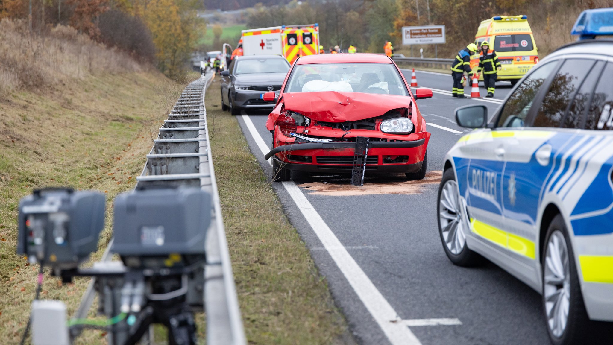 Einsatzkräfte von Polizei und Rettungsdienst stehen neben Unfallautos auf einer Bundesstraße bei Coburg.