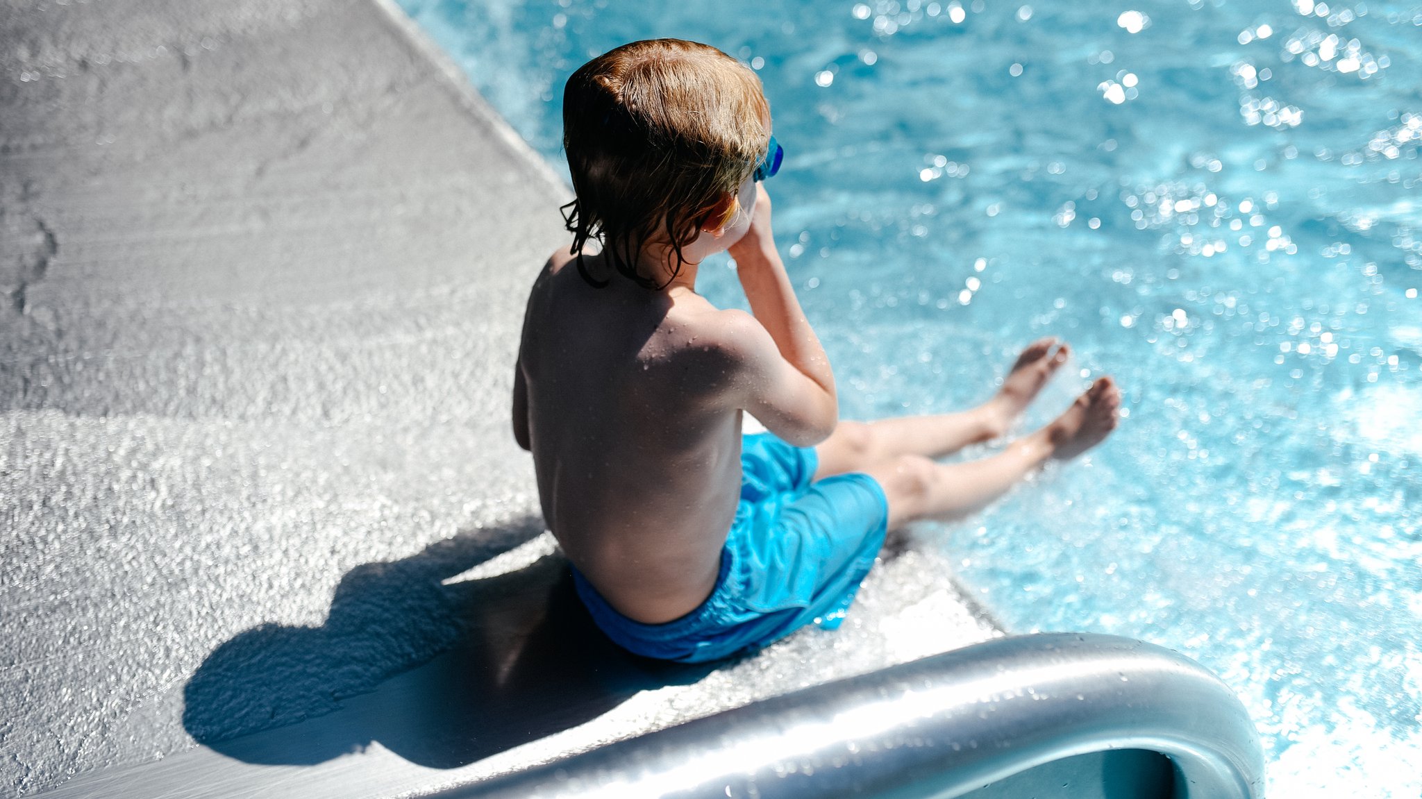 Kleiner Junge rutscht auf Rutsche ins Wasser.