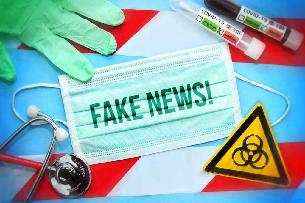 Symbolbild zu "Fake News" mit Maske, Teströhrchen und einem Warnschild für Biogefährdung.