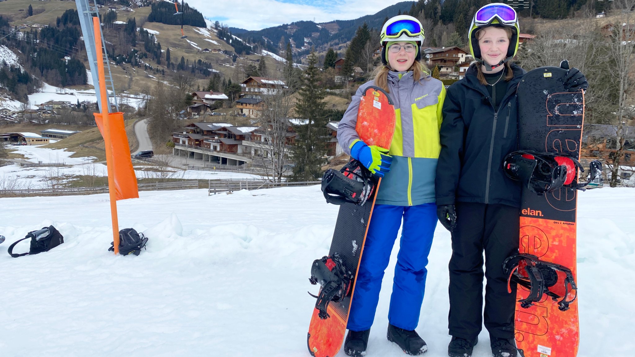 Zwei junge Mädchen stehen mit Snowboard im Schnee