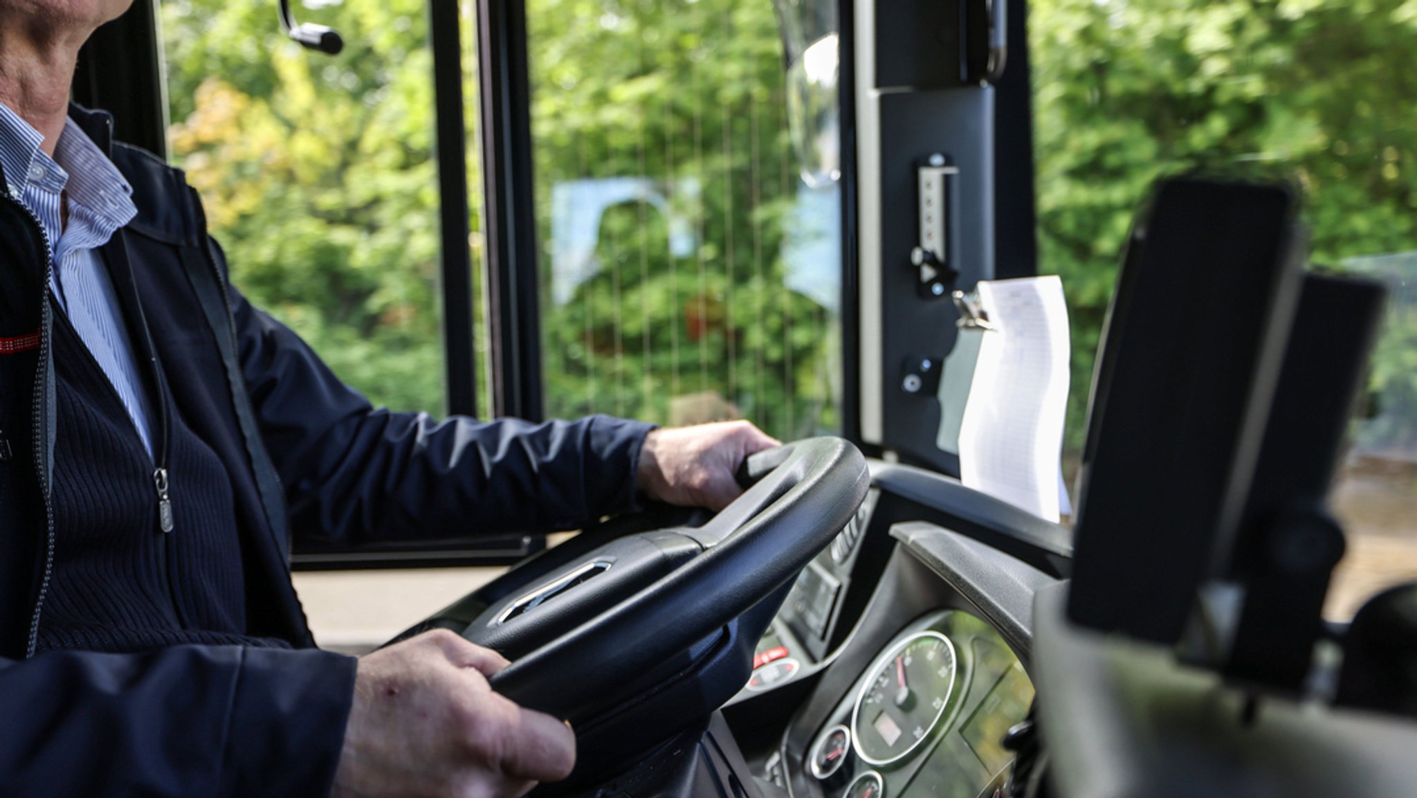 Symbolbild: Hände eines älteren Busfahrers am Lenkrad.