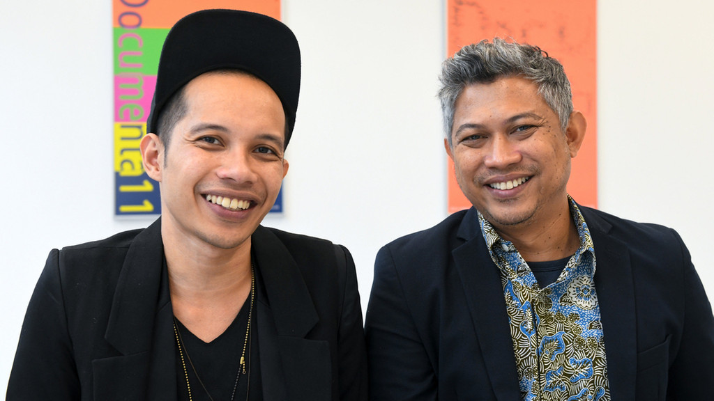 Zwei Mitglieder des indonesischen Künstlerkollektivs Ruangrupa lächeln in die Kamera - vor der documenta fifteen.