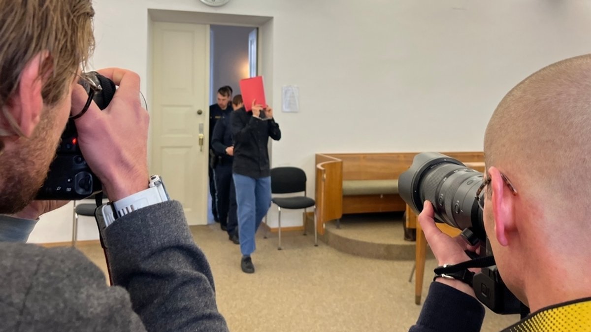 Der Angeklagte betritt mit einer Mappe vor dem Gesicht den Gerichtssaal-