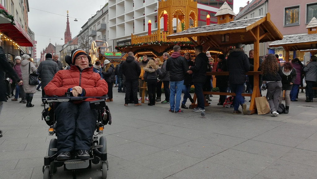 Julian Wendel, Behindertenbeauftragter der Stadt, in seinem Rollstuhl vor einem Glühweinstand am Würzburger Weihnachtsmarkt. 