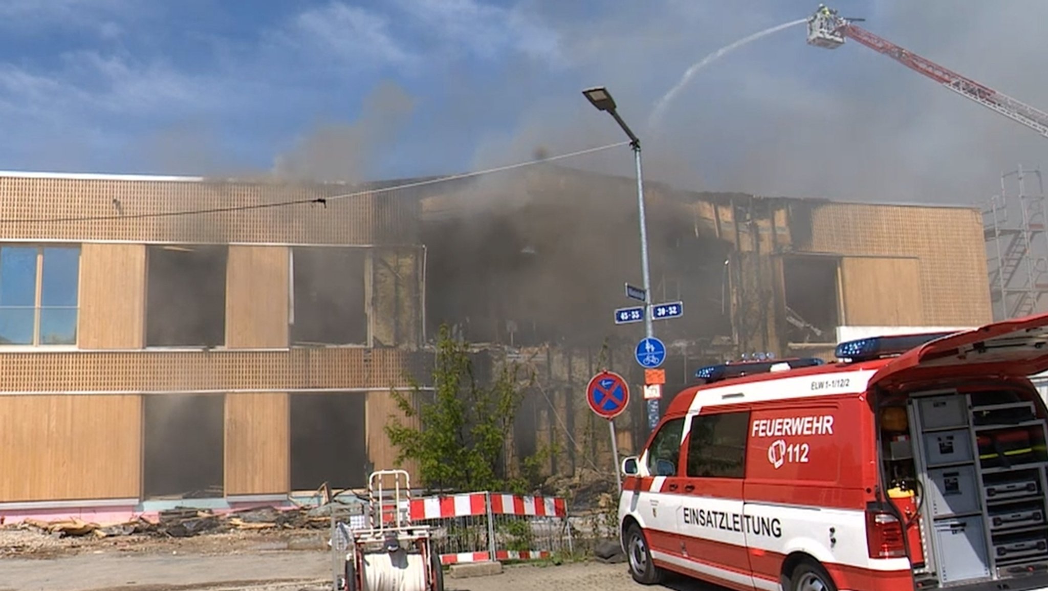 Feuerwehrauto vor einem brennenden Gebäude, aus dem schwarzer Rauch quillt