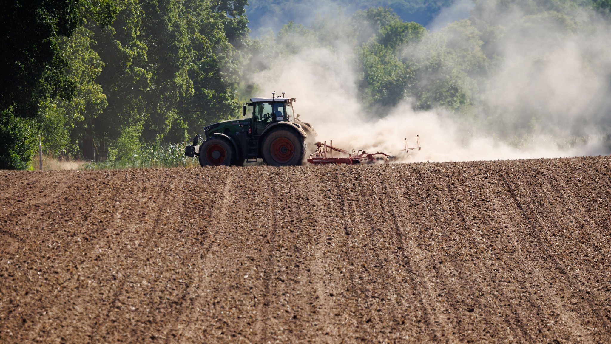 13.08.2026, Bayern, Pleinfeld: Ein Landwirt bearbeitet mit seinem Traktor ein abgeerntetes Getreidefeld und wirbelt dabei Staub vom trockenen Boden auf. Foto: Daniel Karmann/dpa +++ dpa-Bildfunk +++