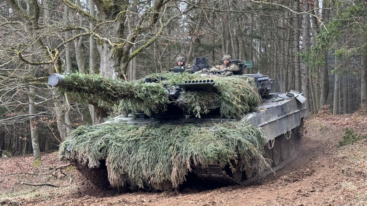 Ein mit Zweigen getarnter Panzer fährt durch einen Wald auf dem Truppenübungsplatz Hohenfels.