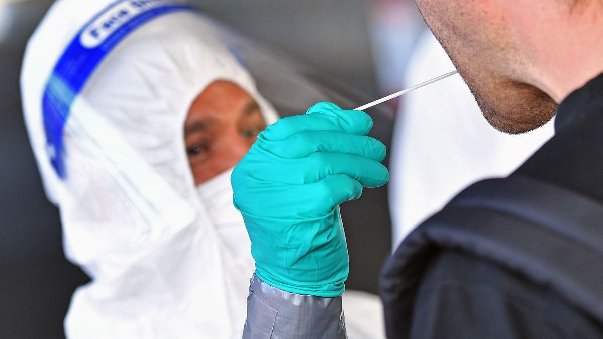 Ein Mitarbeiter eines Testzentrums macht einen Rachenabstrich bei einem Mann.