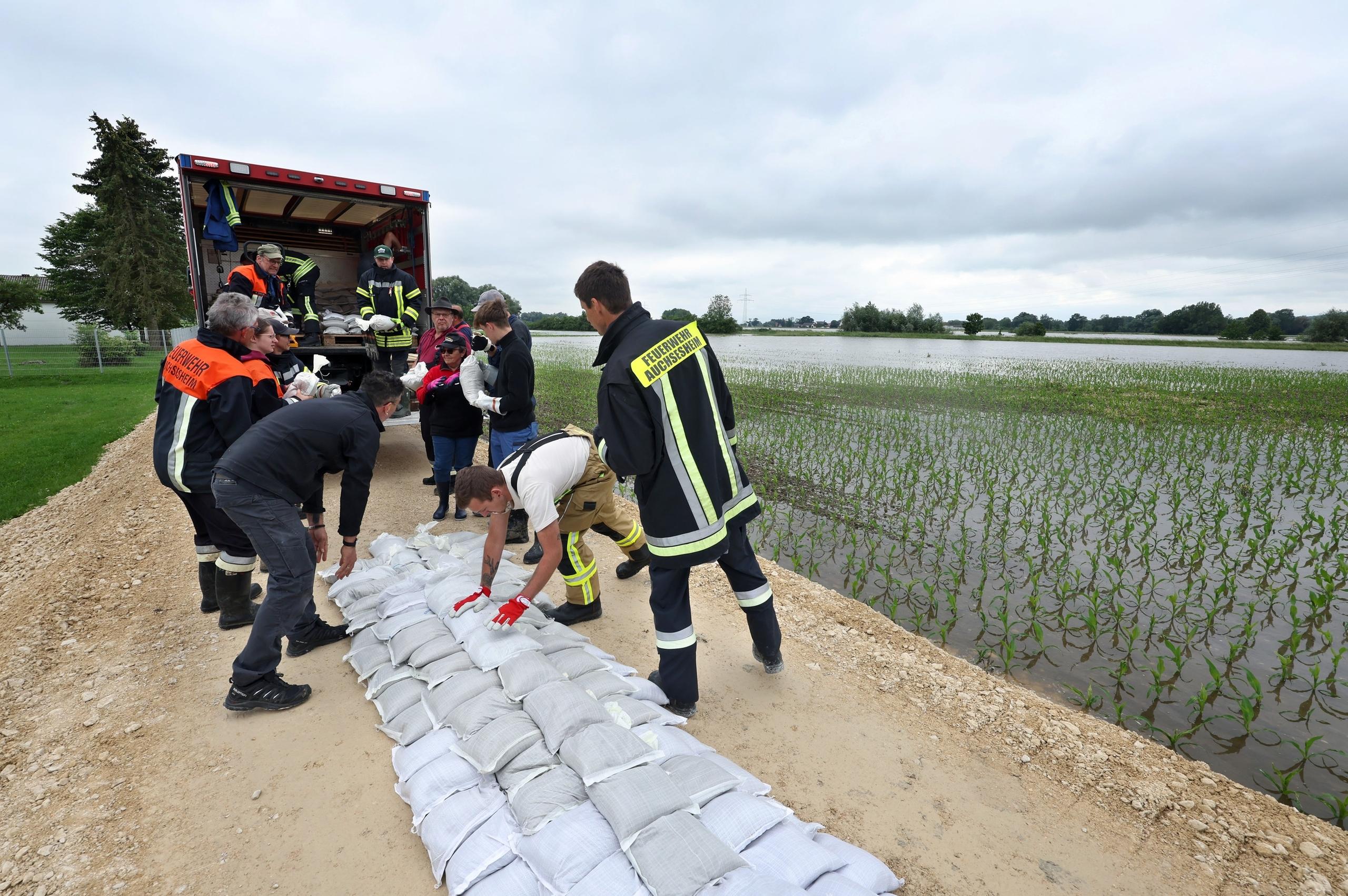 03.06.2024, Bayern, Donauwörth: Feuerwehrleute und freiwillige Helfer befestigen im Ortsteil Auchsesheim nach einem Dammbruch einen zweiten Damm mit Sandsäcken um das Hochwasser der Zusam zu stoppen. Seit Tagen kämpfen die Helfer in Bayern und Baden-Württemberg gegen die Flut und ihre Folgen. Die Hochwasserlage ist weiter dynamisch und unübersichtlich. Viele kleine Gemeinden sind betroffen, mancherorts spitzt sie sich die Lage sogar zu. Foto: Karl-Josef Hildenbrand/dpa +++ dpa-Bildfunk +++