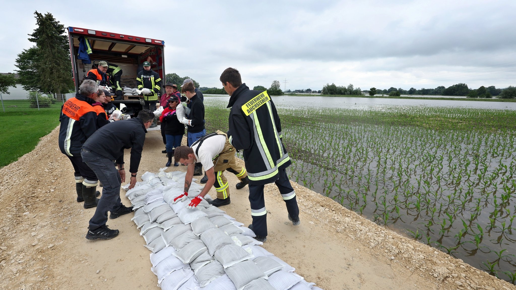 03.06.2024, Bayern, Donauwörth: Feuerwehrleute und freiwillige Helfer befestigen im Ortsteil Auchsesheim nach einem Dammbruch einen zweiten Damm mit Sandsäcken um das Hochwasser der Zusam zu stoppen. Seit Tagen kämpfen die Helfer in Bayern und Baden-Württemberg gegen die Flut und ihre Folgen. Die Hochwasserlage ist weiter dynamisch und unübersichtlich. Viele kleine Gemeinden sind betroffen, mancherorts spitzt sie sich die Lage sogar zu. Foto: Karl-Josef Hildenbrand/dpa +++ dpa-Bildfunk +++