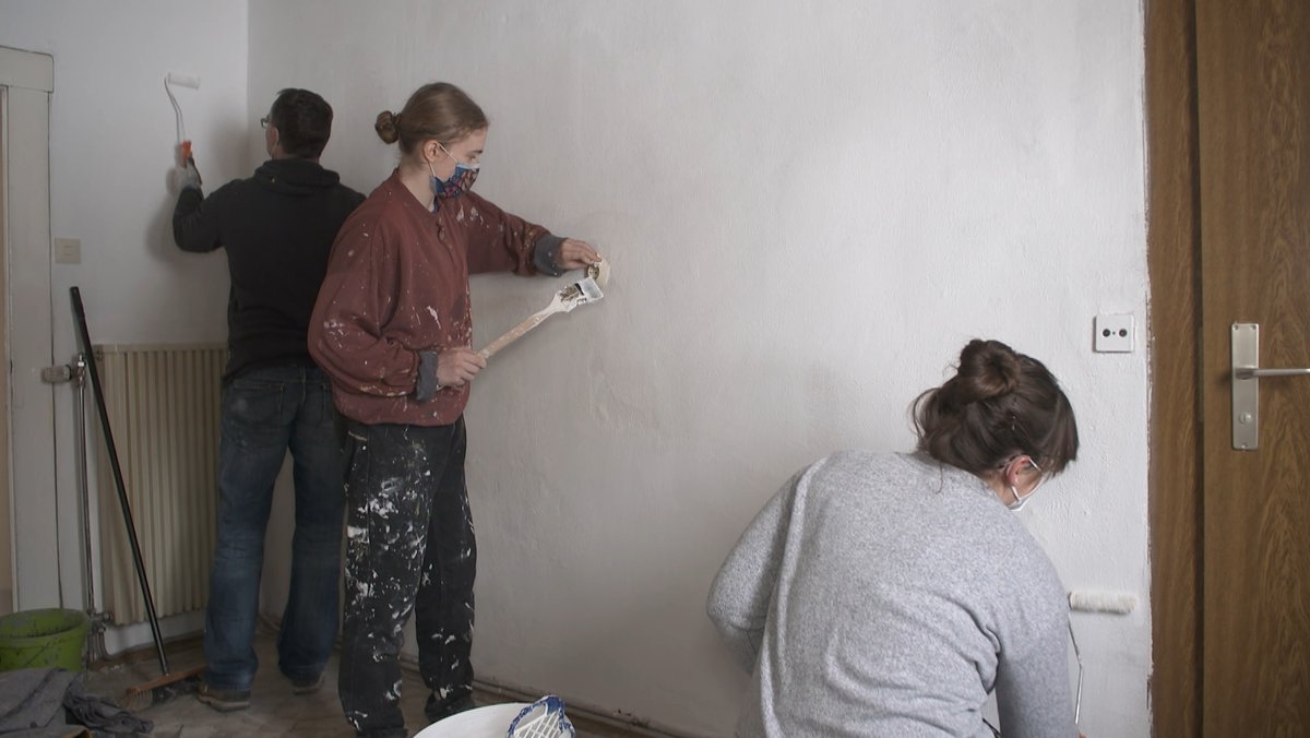Zwei Frauen und ein Mann streichen Wände.
