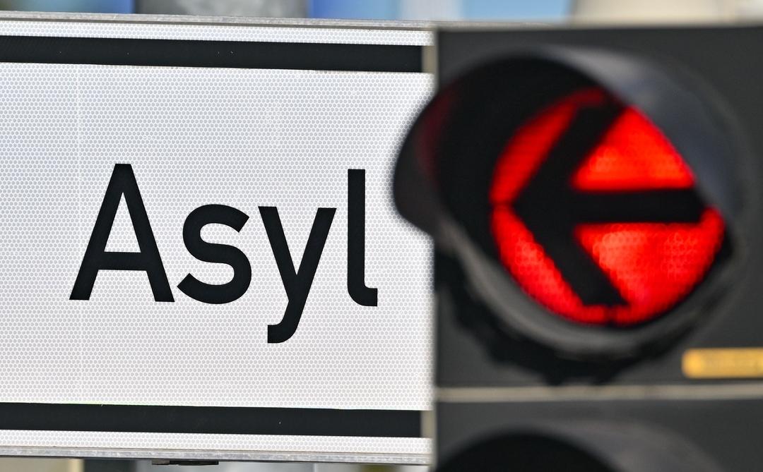 Eine rote Ampel leuchtet vor dem Wort "Asyl" auf einem Wegweiser zu einer Erstaufnahme-Einrichtung